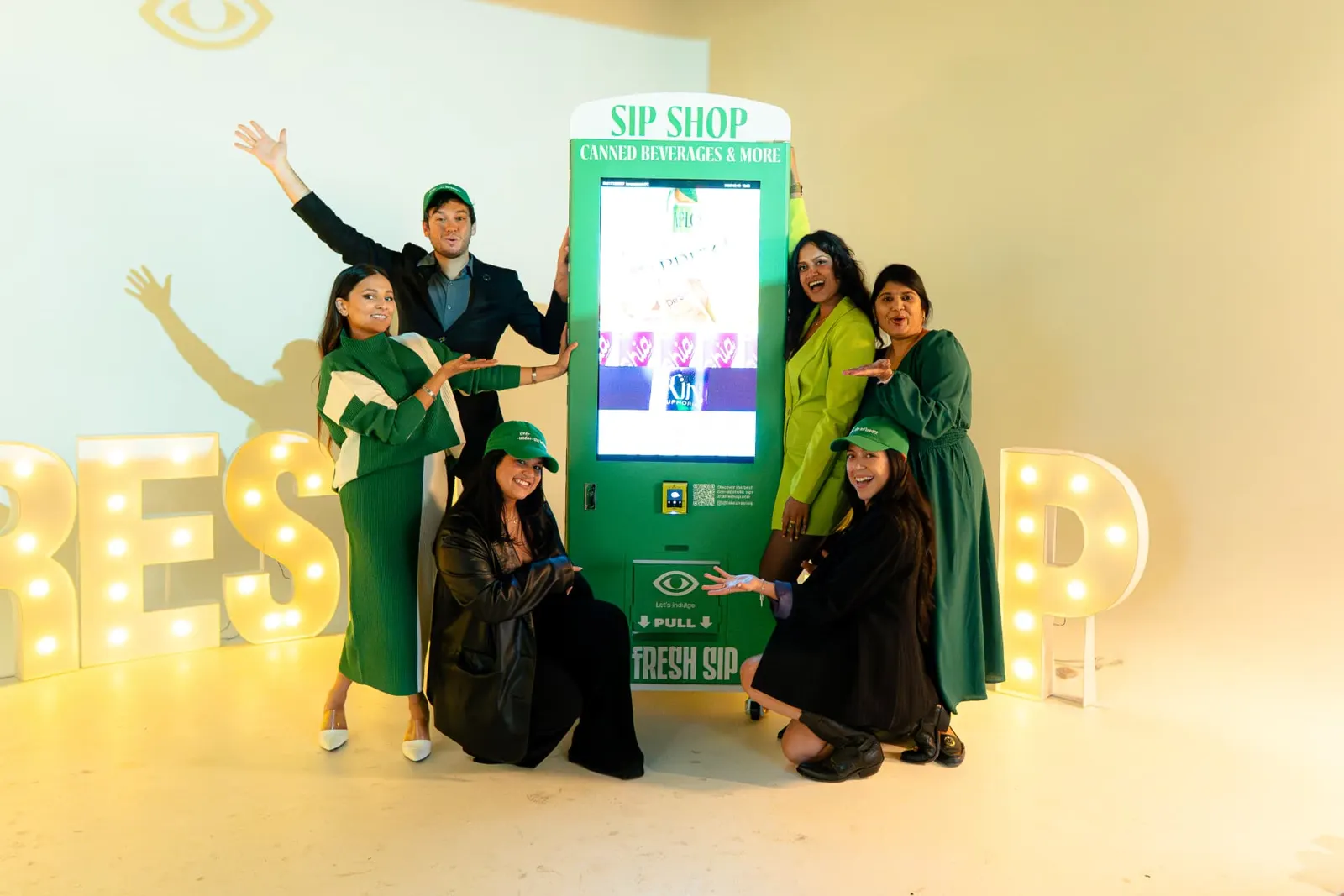A Fresh Sip team posing around the branded Sip Shop vending machine